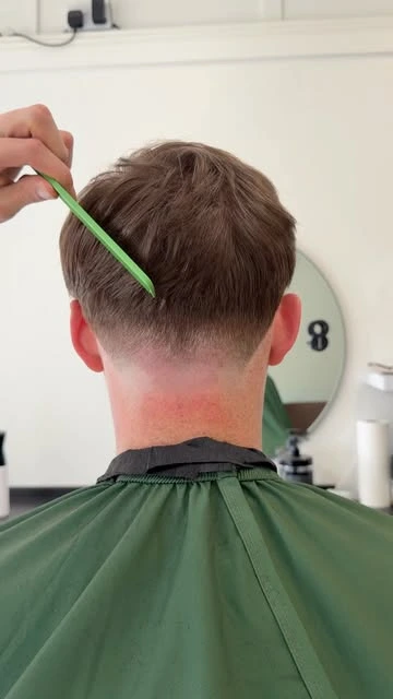 Rab using a green comb to refine a skin fade