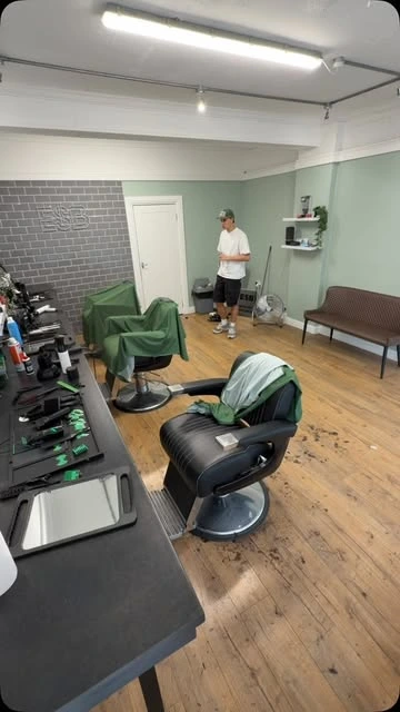 The Escobarber studio: sage walls, green barber capes and wood flooring